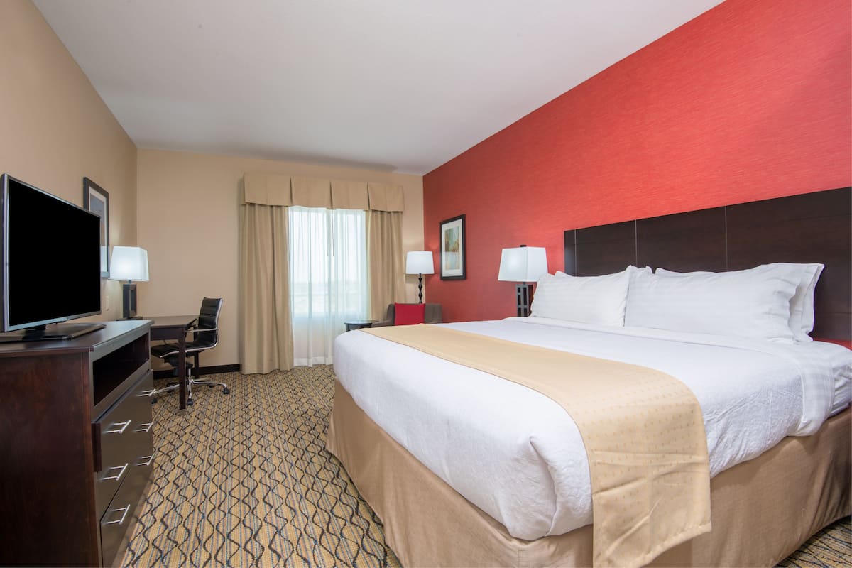 A hotel room with a large bed, a desk with a chair, a television, and a window with curtains.