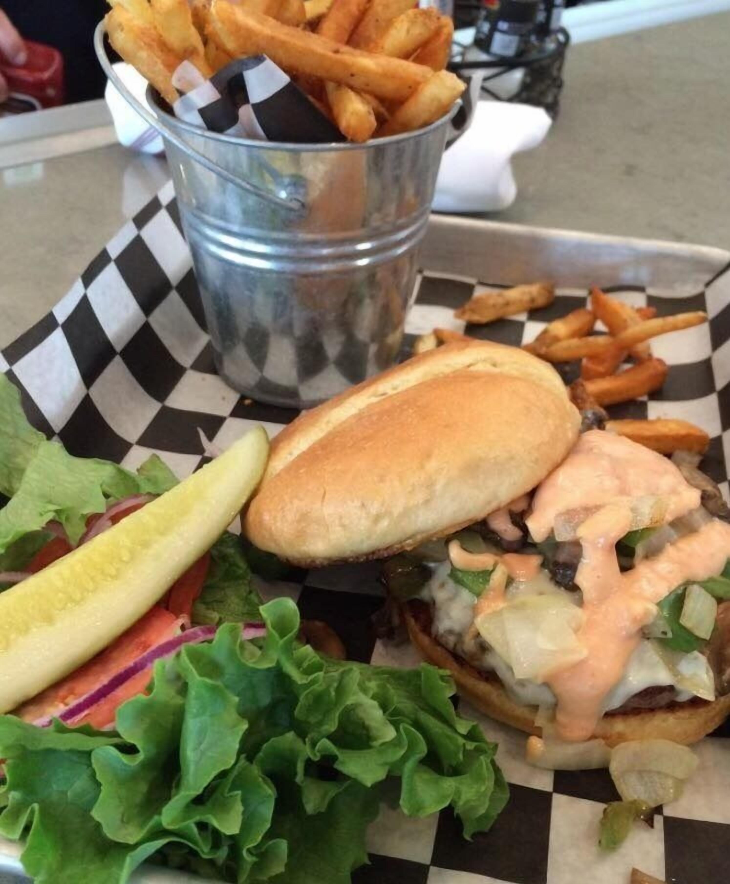A burger with lettuce, a pickle, and a side of fries on a checkered paper.