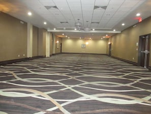 Un salón de conferencias amplio y vacío, con alfombra estampada, iluminación empotrada y una pared lisa con una puerta a la derecha.
