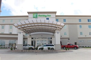 Un hotel Holiday Inn con entrada cubierta, varios espacios de estacionamiento y cielo despejado.