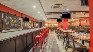 A restaurant with a long counter, red stools, and multiple tables.