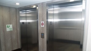 Dues portes d'ascensor en un passadís amb un terra estampat i un senyal que indica l'ús d'escales en cas d'incendi.