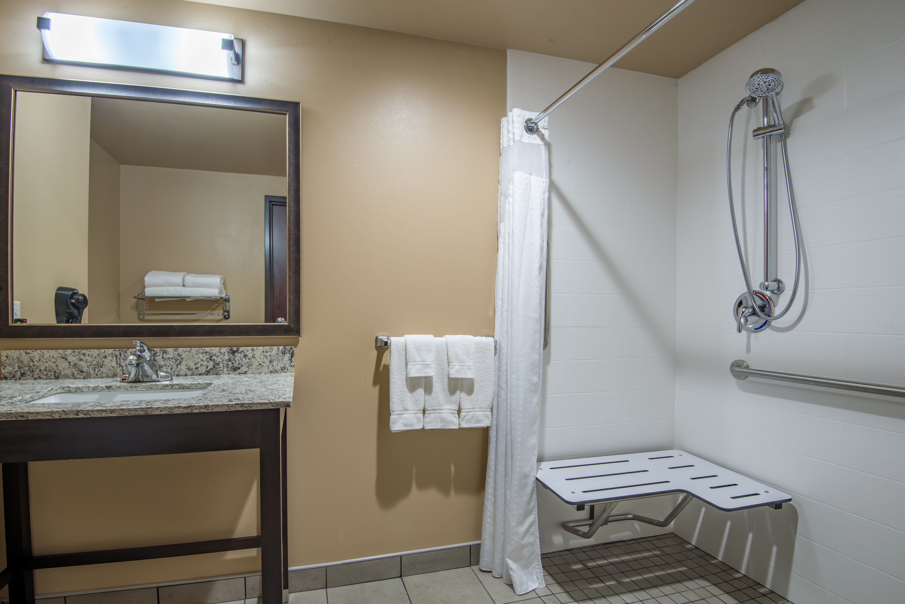 A bathroom with a sink, mirror, towel rack, shower, and grab bar.
