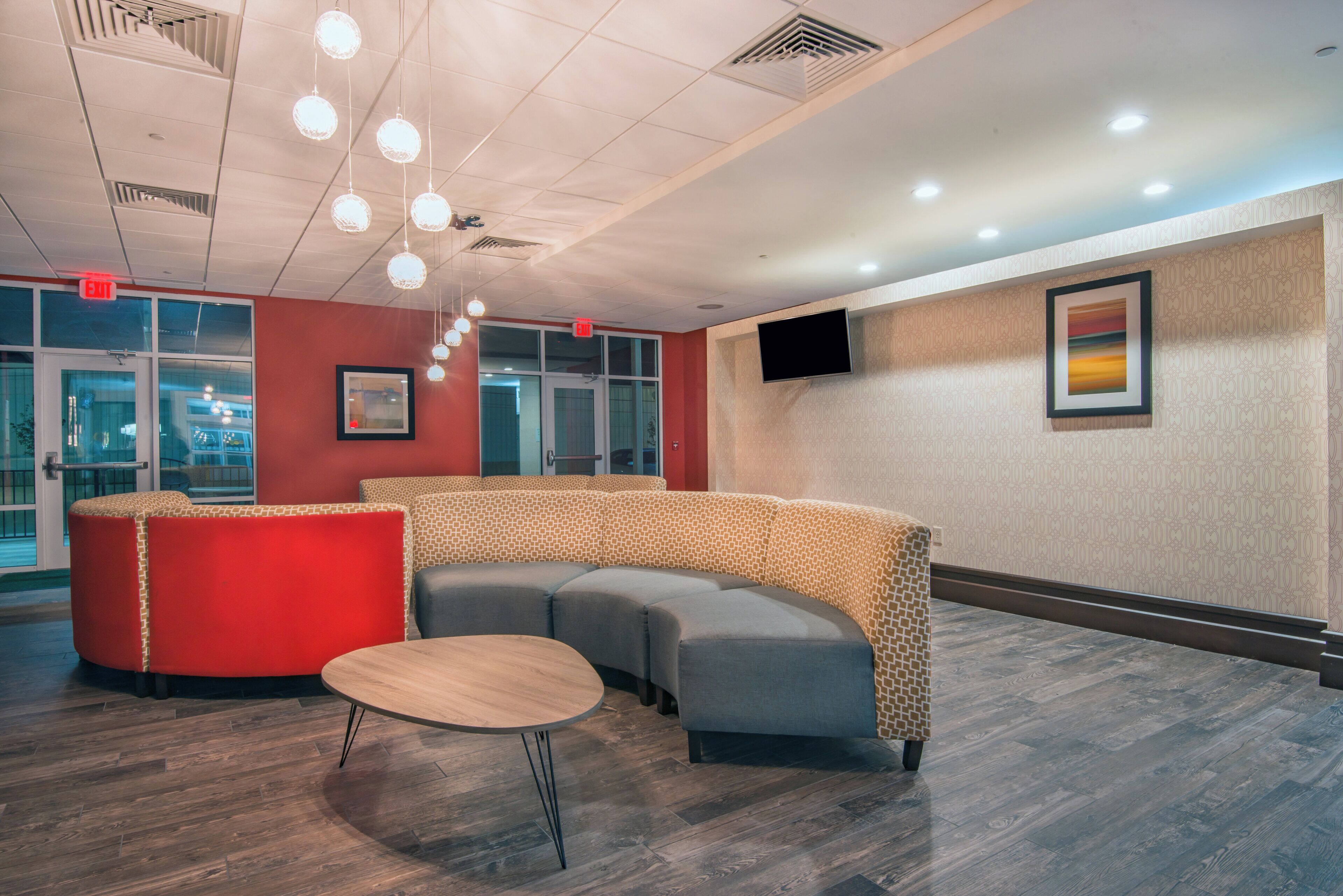 A modern waiting area with a curved seating arrangement, a round table, and a flat-screen TV mounted on the wall.