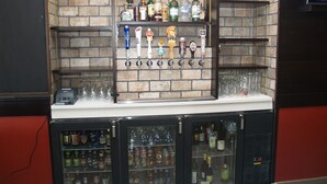 Zona de bar amb paret de maó, nombroses prestatgeries plenes de botelles i un vitrina refrigerada.