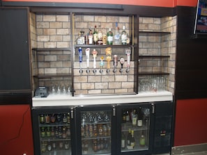 Zona de bar con pared de ladrillo, varias estanterías llenas de botellas y un expositor refrigerado.