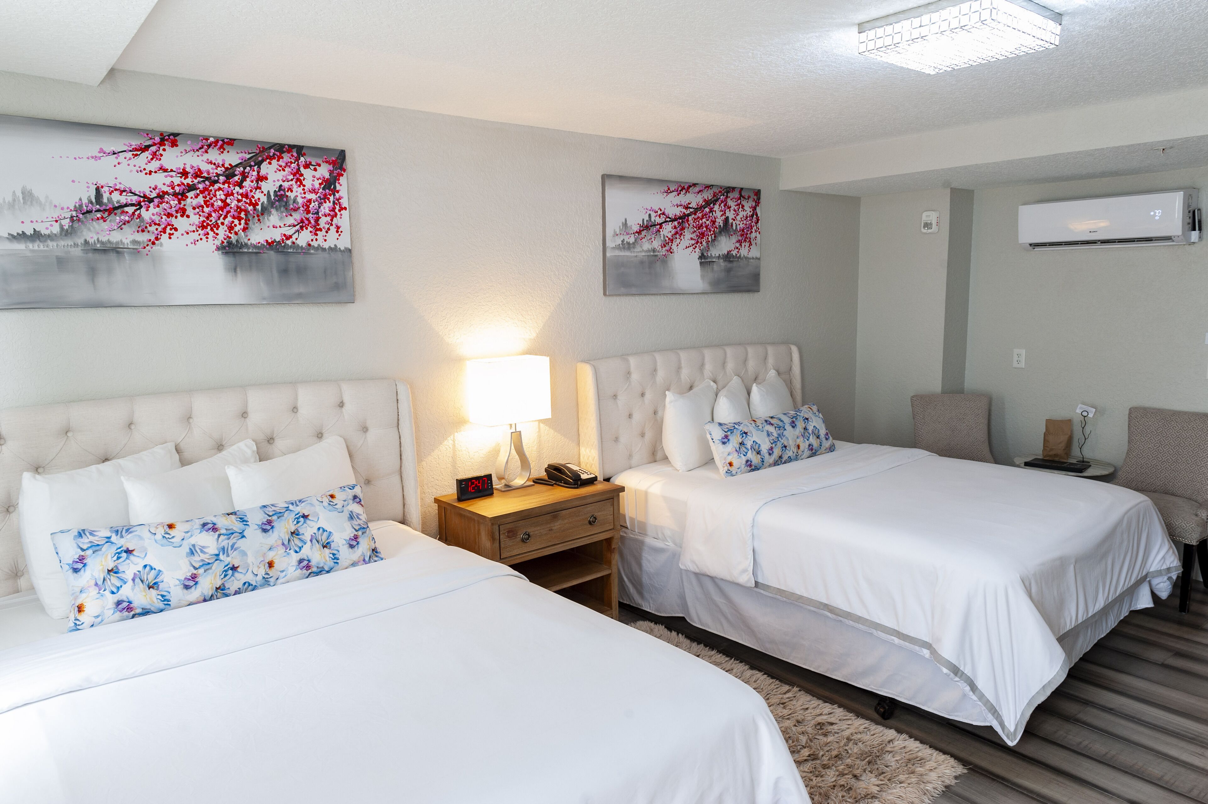 A hotel room with two beds, a nightstand, a lamp, and artwork on the walls.