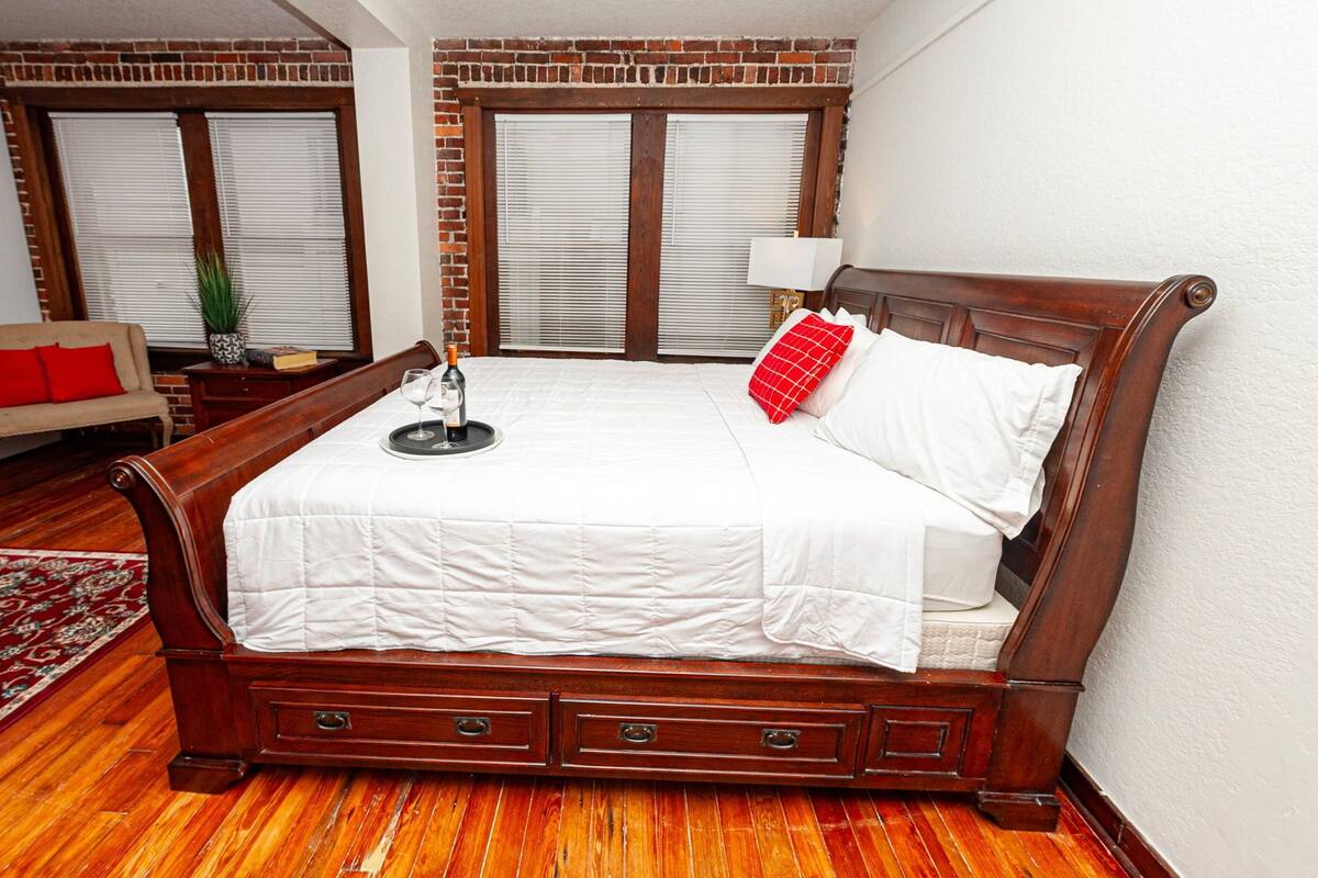 A bedroom with a large wooden bed, a bench, a small table with a tray, and a red pillow.