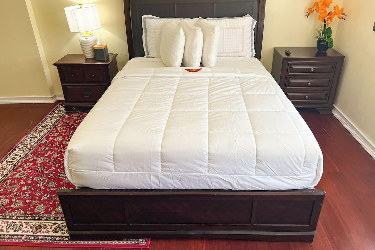 A neatly made bed with white bedding, a dark headboard, and a red patterned rug.