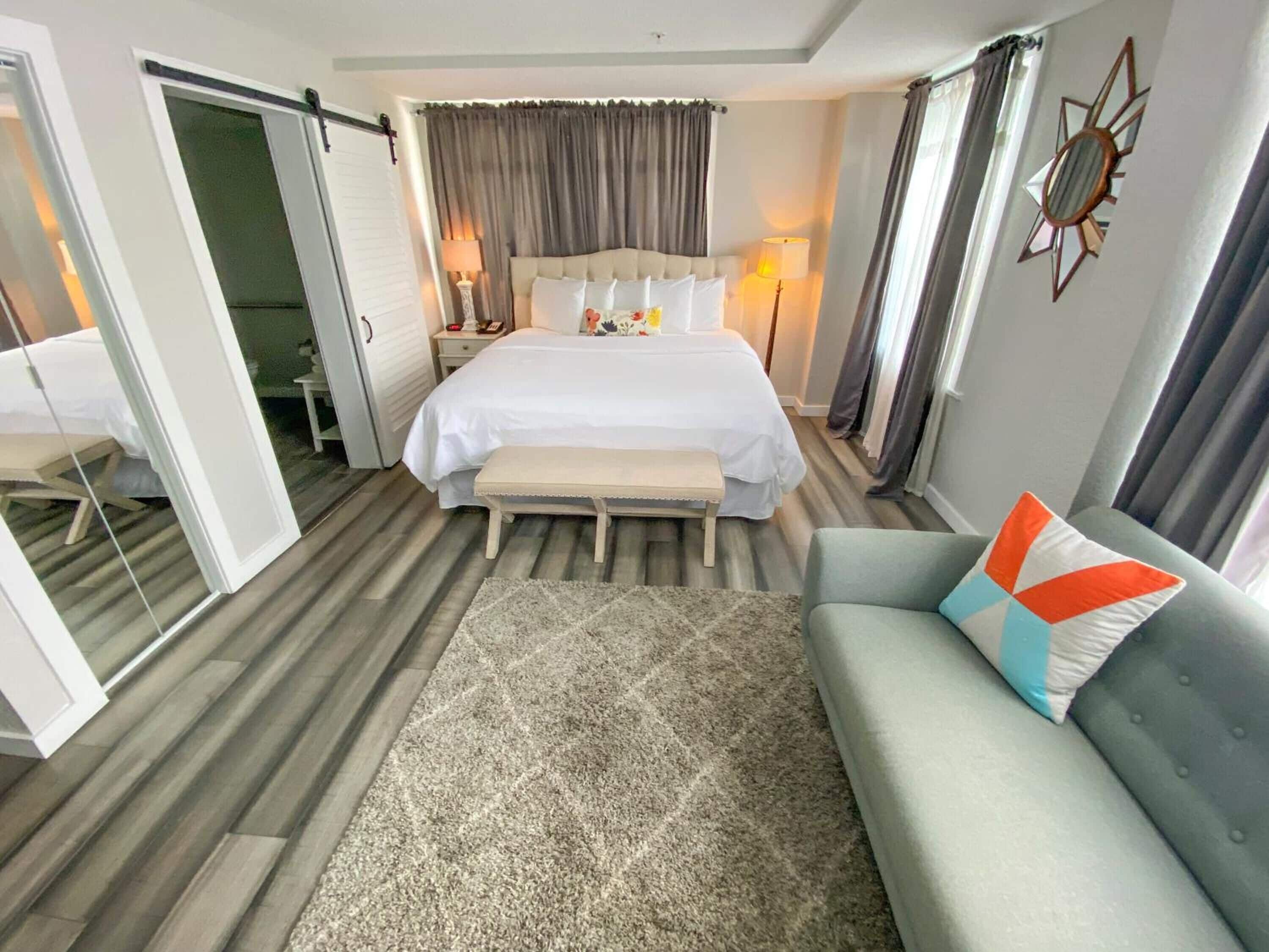 A hotel room with a large bed, a bench, a sofa, a mirror, and a nightstand with lamps.