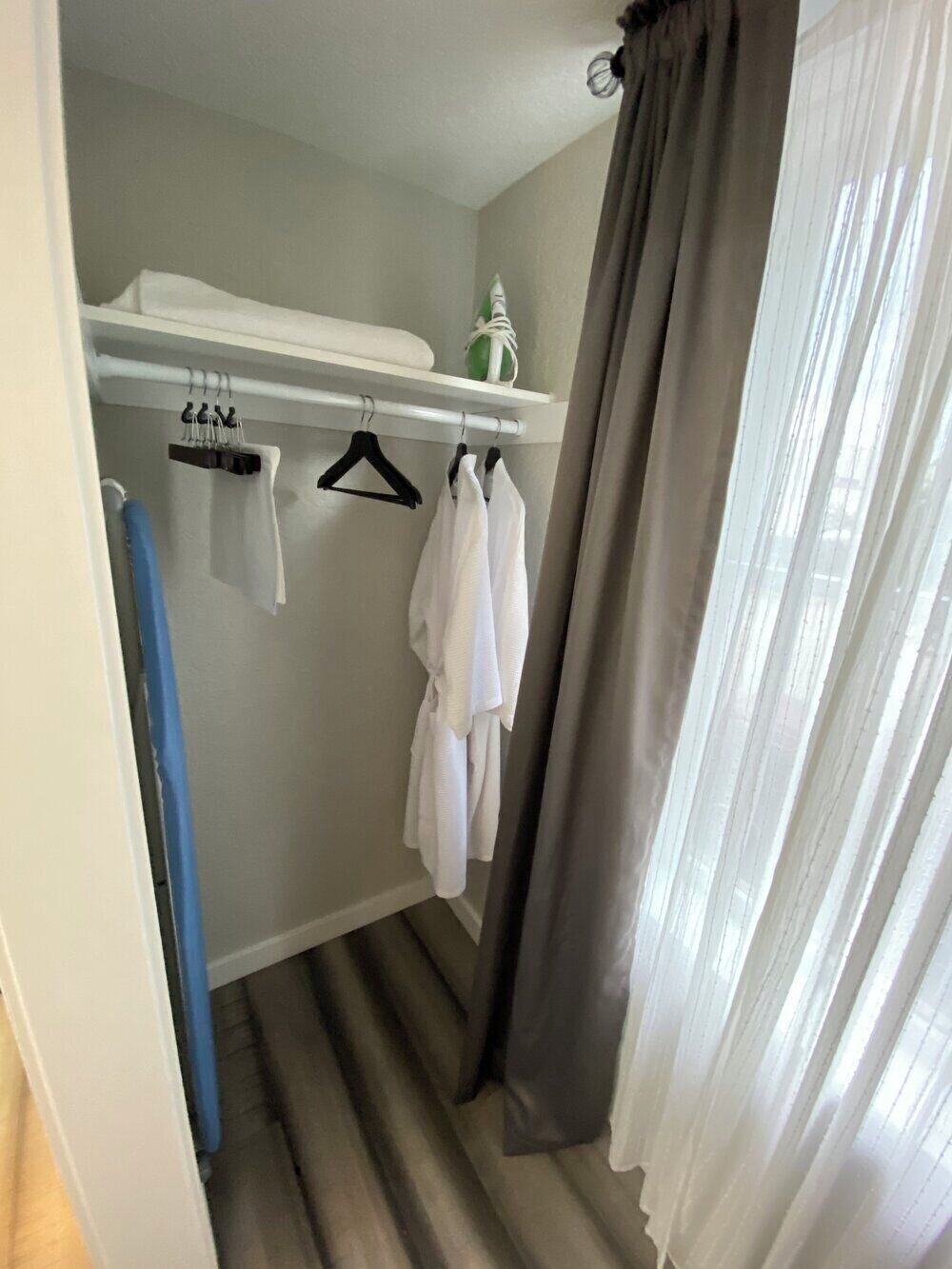A room with a white ceiling, a white shelf with hangers, a blue curtain, and a grey curtain.