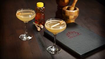 Two cocktails on a dark wooden table with a honey bottle and a wooden mortar and pestle.