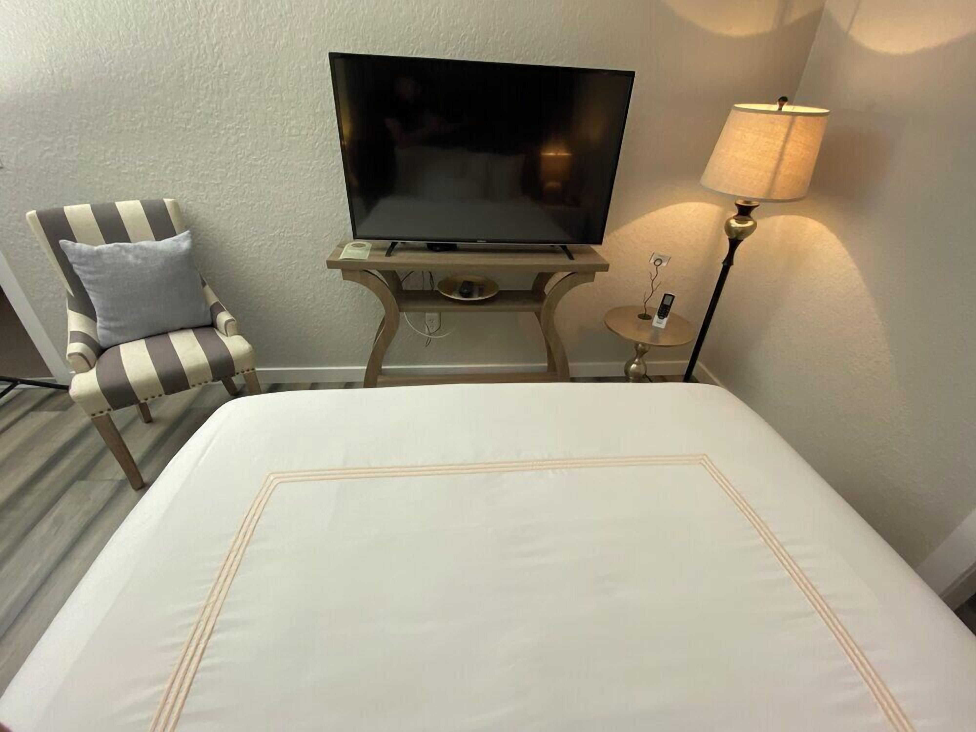A hotel room with a bed, a television on a stand, a chair, and a lamp.