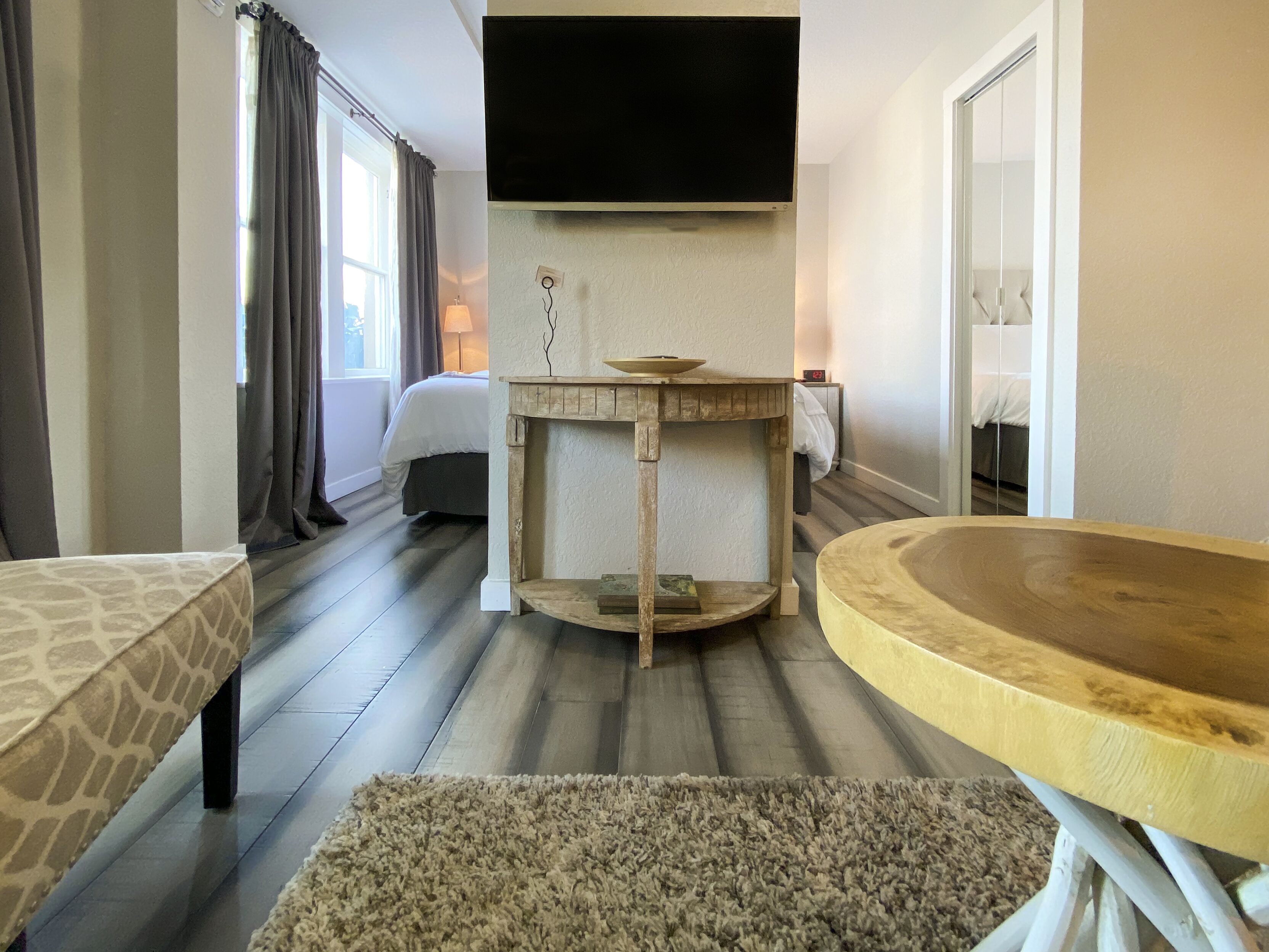 A hotel room with a bed, a TV mounted on the wall, a wooden side table, and a round wooden table.