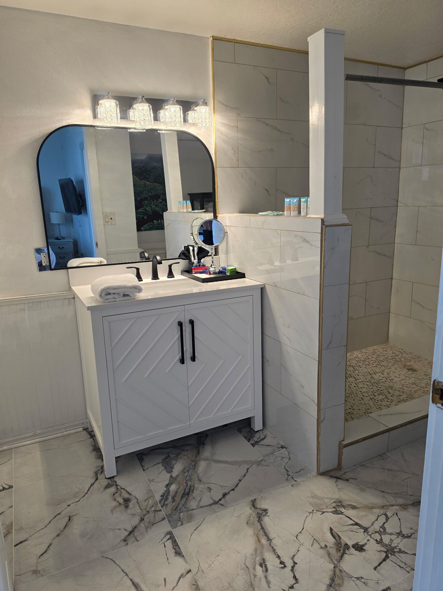 A bathroom with a white vanity, a large mirror, and a shower area.