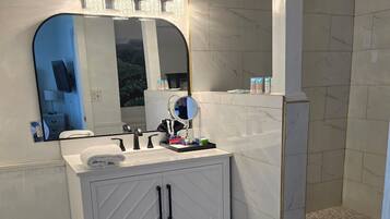 A bathroom with a white vanity, a large mirror, and a shower area.