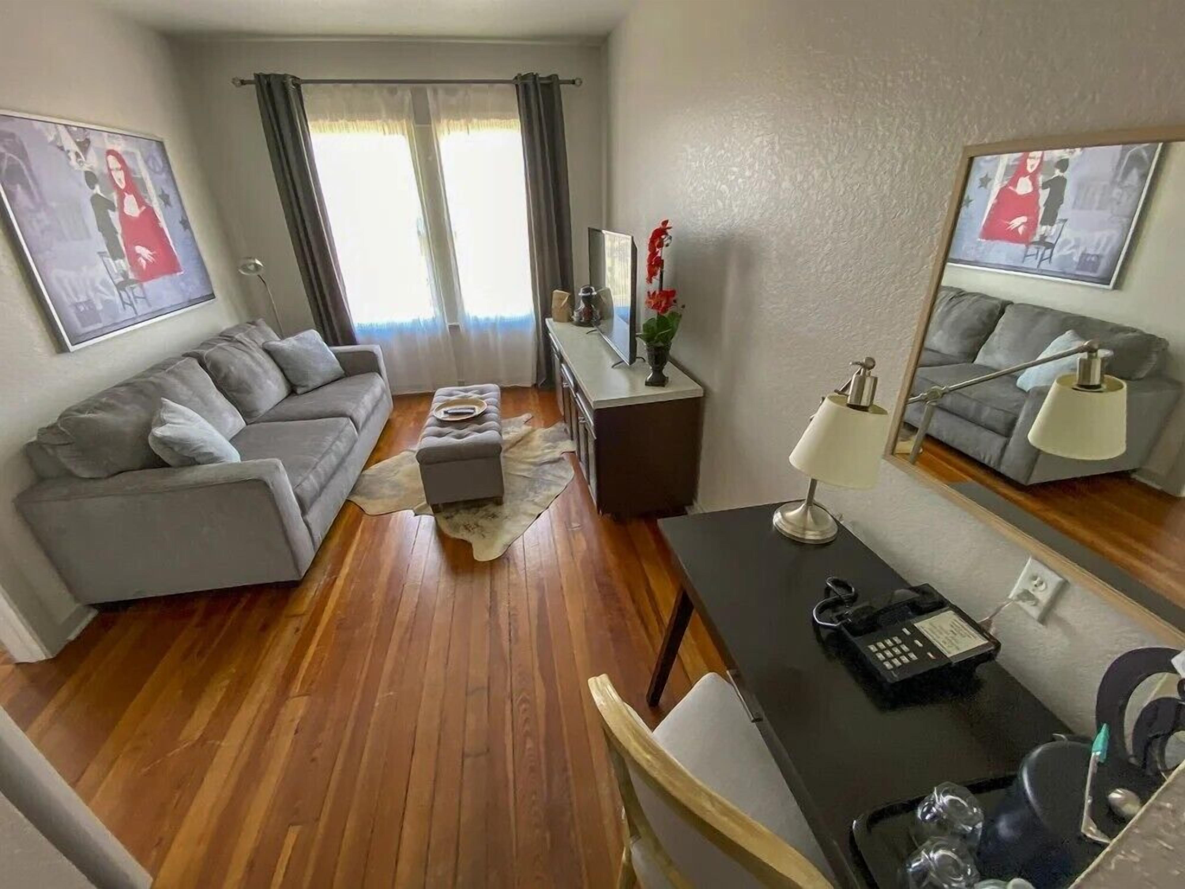 Una sala de estar moderna con un sofá gris, una mesa de comedor con una lámpara y una mesita auxiliar.