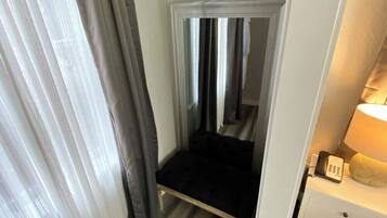 A narrow room with a bed, a nightstand with a lamp, and a door leading to another room.