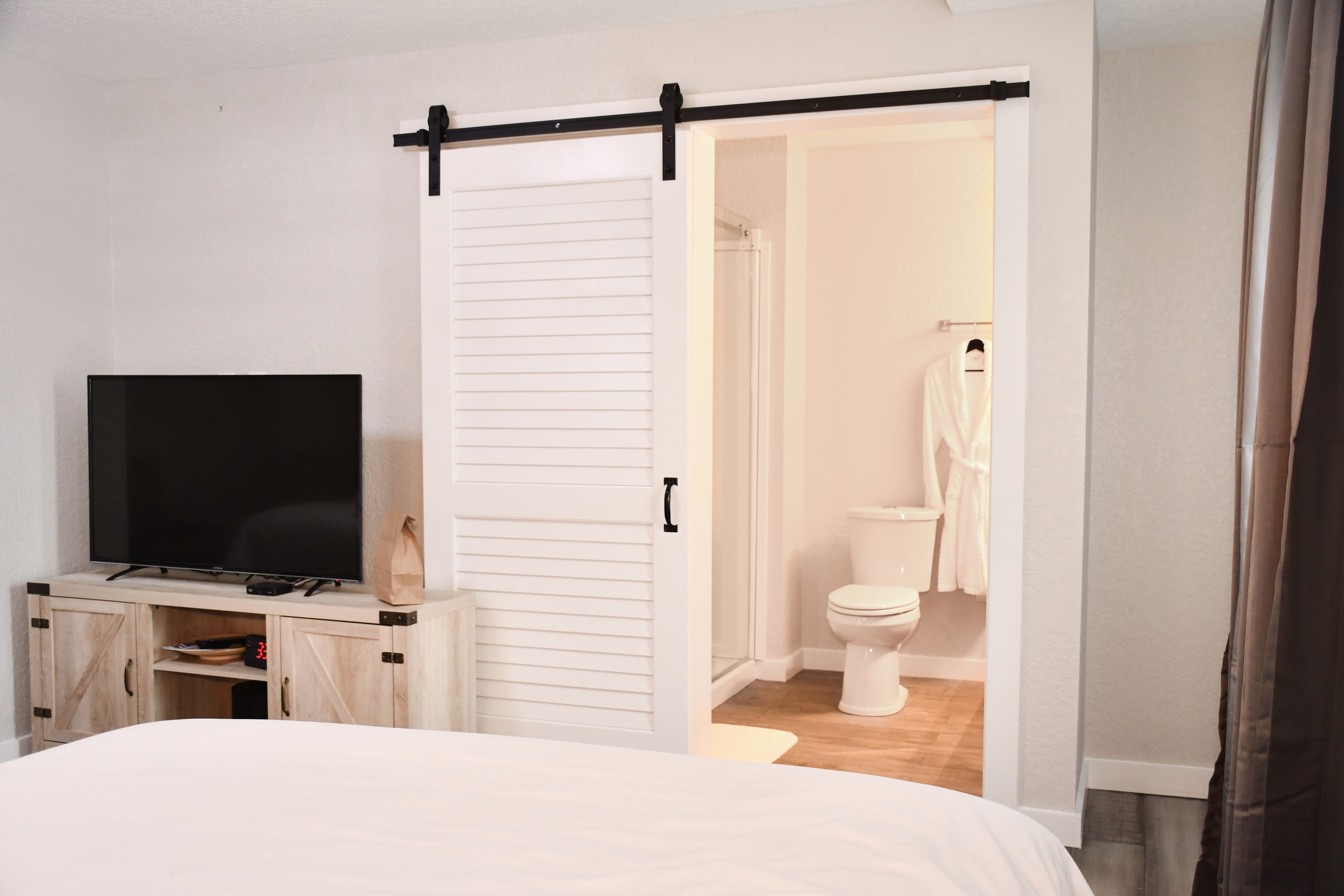 A bedroom with a bed, a TV on a wooden cabinet, a sliding door to a bathroom, and a white wardrobe.