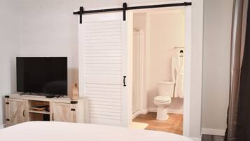 A bedroom with a bed, a TV on a wooden cabinet, a sliding door to a bathroom, and a white wardrobe.