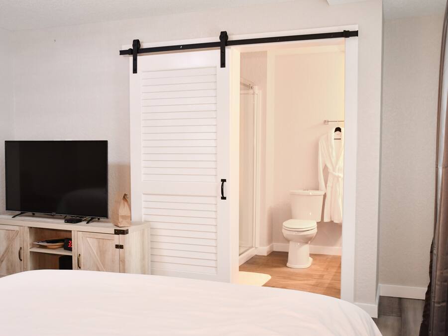 A bedroom with a bed, a TV on a wooden cabinet, a sliding door to a bathroom, and a white wardrobe.