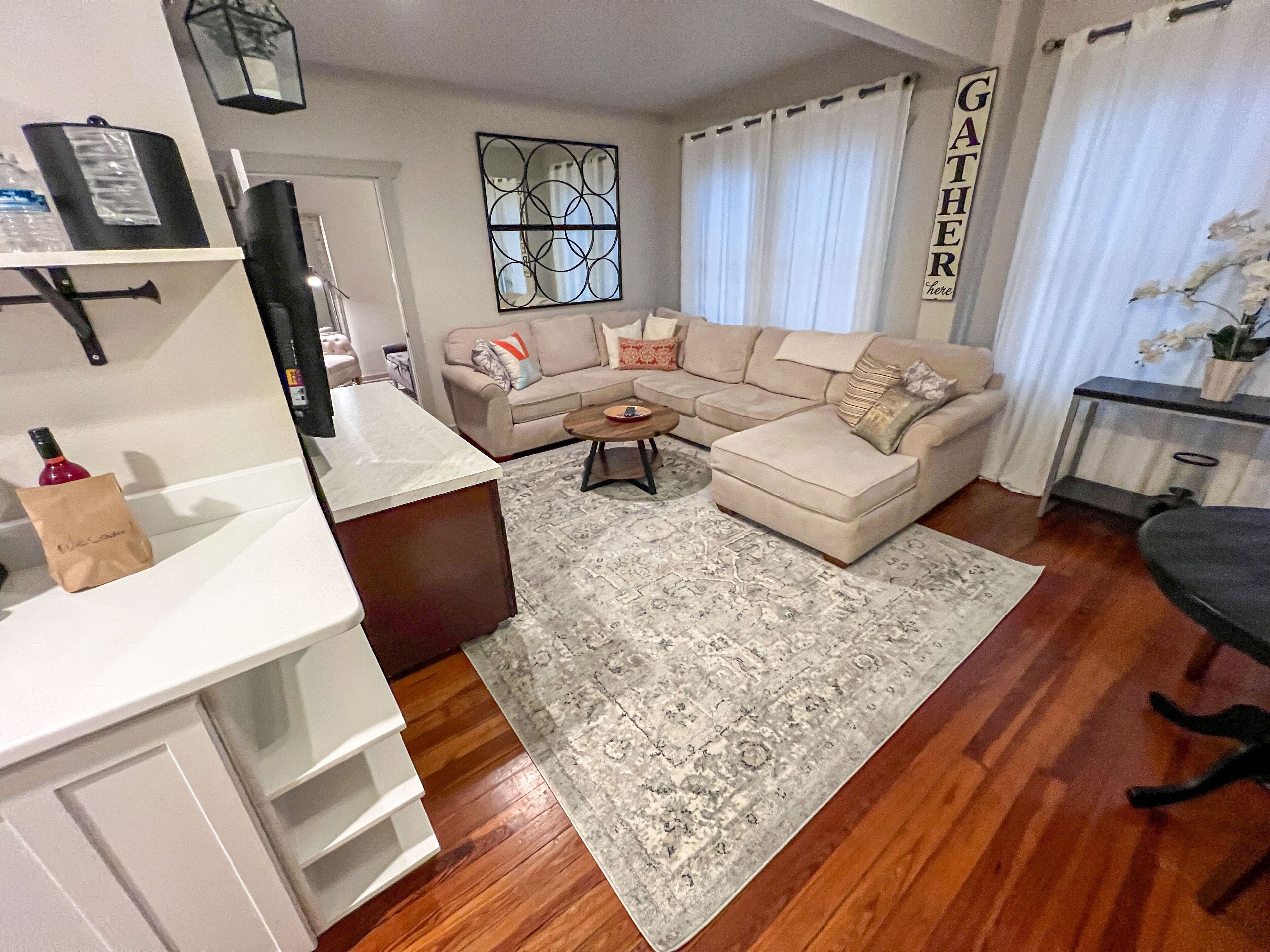 Ein Wohnzimmer mit einem beigefarbenen Ecksofa, einem Couchtisch, einem Teppich und einem Fernseher auf einem Lowboard.
