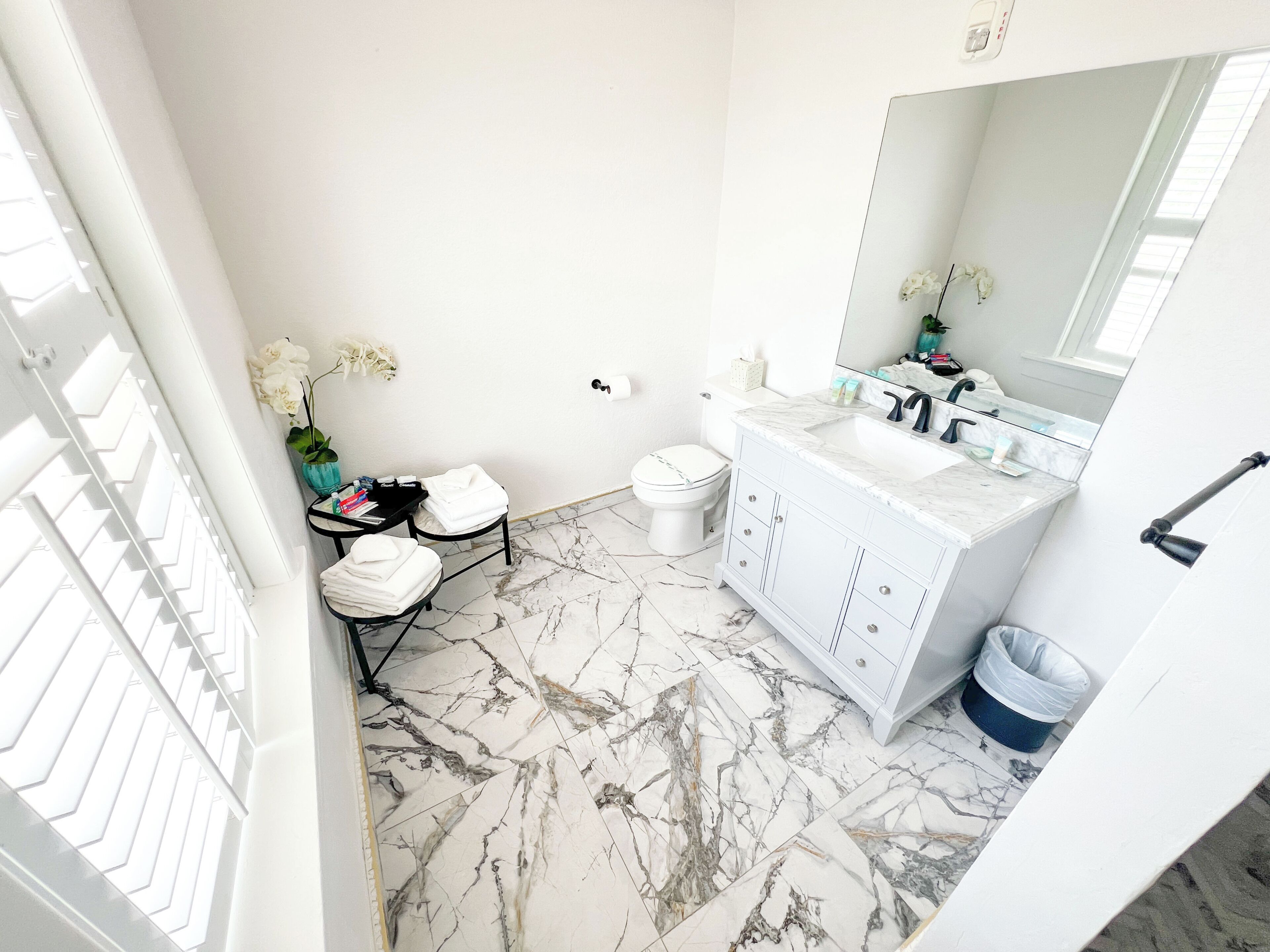 Une salle de bain avec un meuble-lavabo blanc, un sol en marbre et un grand miroir.