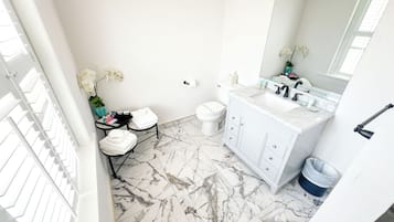 Une salle de bain avec un meuble-lavabo blanc, un sol en marbre et un grand miroir.