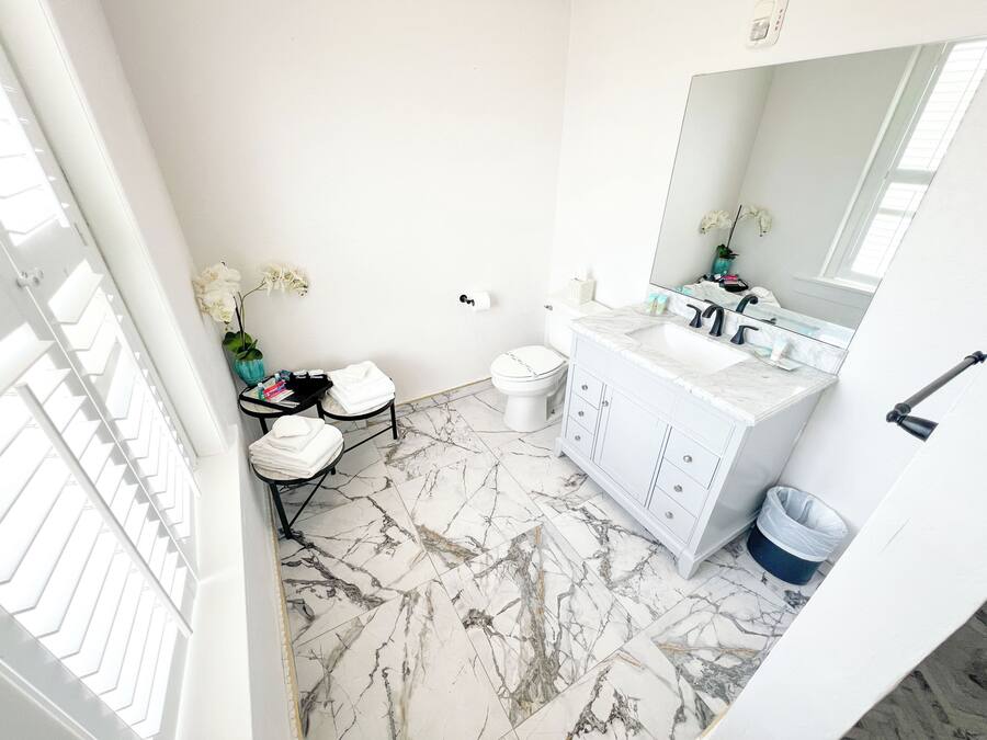Une salle de bain avec un meuble-lavabo blanc, un sol en marbre et un grand miroir.