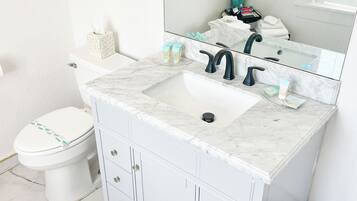 A bathroom with a white marble sink, a toilet, and a vanity with drawers.