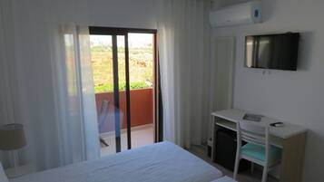 A hotel room with a bed, a desk, a TV, and a balcony with a view of the city.