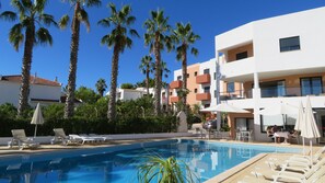 Ein Swimmingpool mit Liegestühlen, Palmen und einem modernen Gebäude mit Balkonen.