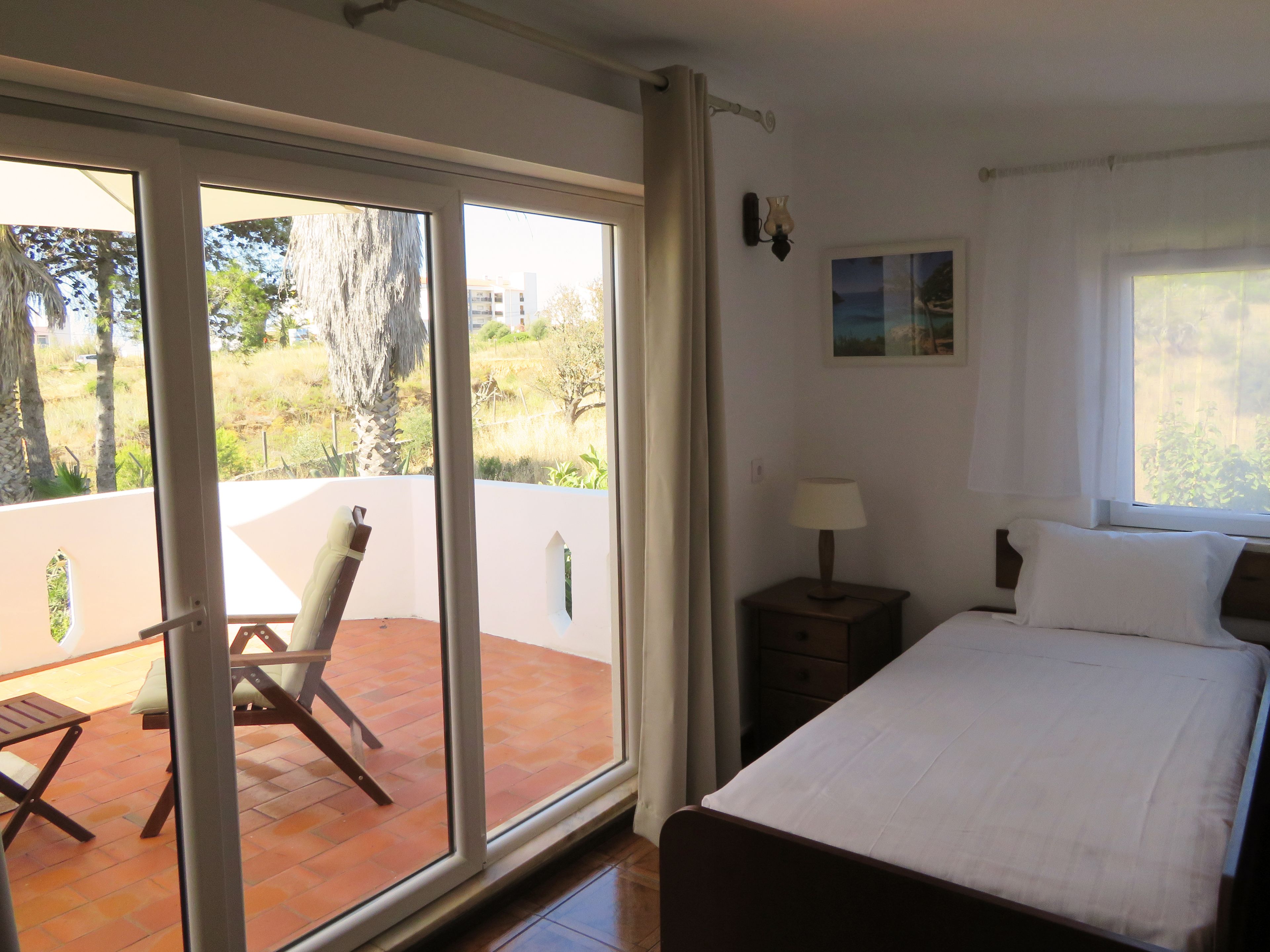 A bedroom with a bed, a nightstand, a chair, and a view of the outdoors through a sliding door.