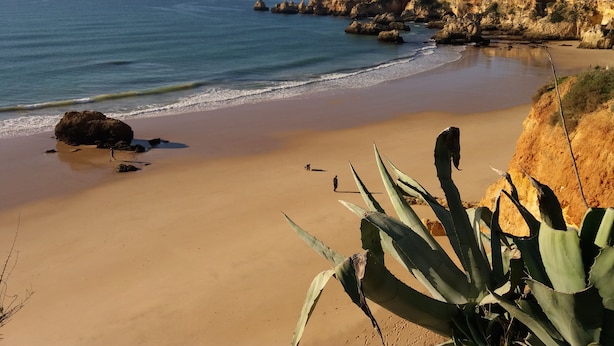 Ein Strand mit klarem, blauem Wasser, Sandstrand und felsigen Klippen.