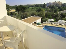 A balcony with a pool, white chairs, and umbrellas.
