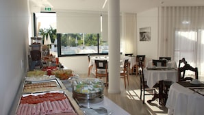 Ein reichhaltiges Buffet mit verschiedenen Speisen, darunter Fleisch- und Käseplatten, in einem hellen Raum mit großen Fenstern und Blick ins Freie.