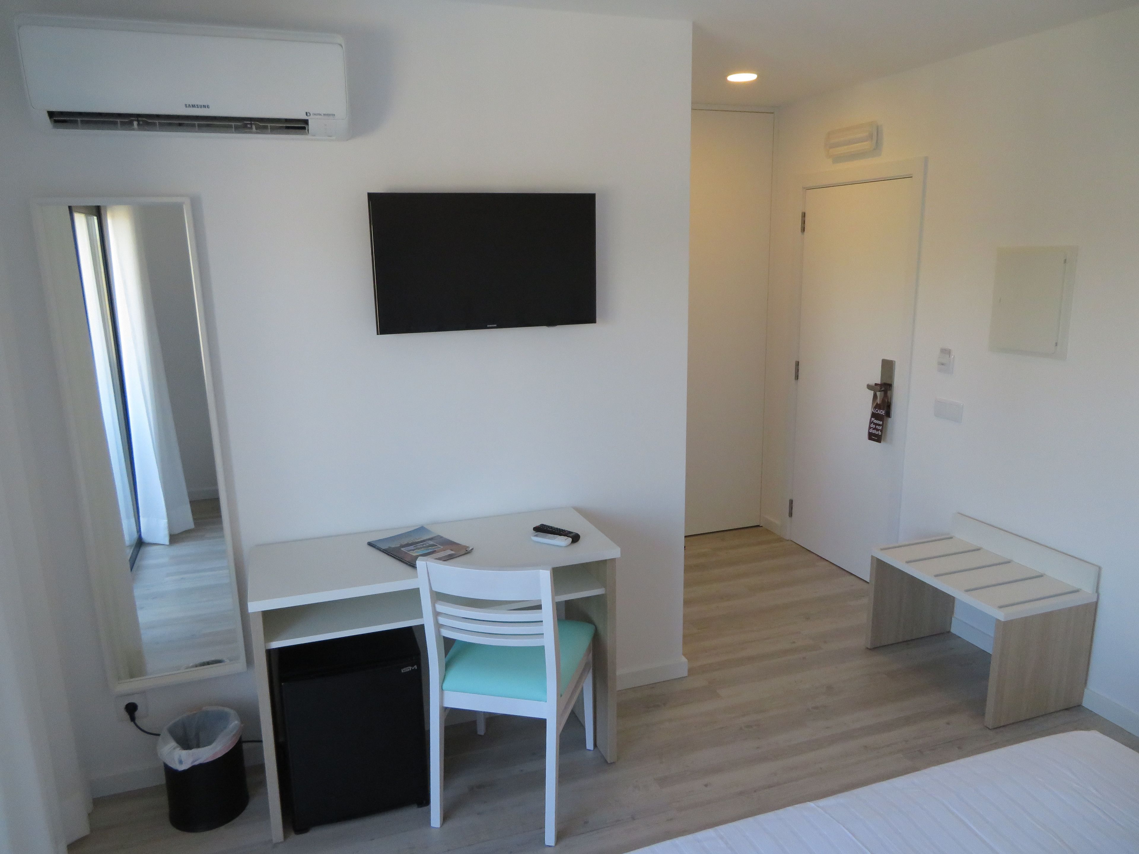 A compact room with a desk, chair, and a television mounted on the wall.