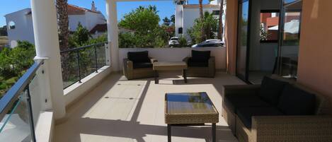 A balcony with wicker furniture, a glass table, and a view of the neighborhood.