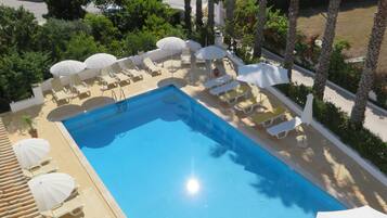 Une piscine rectangulaire entourée de palmiers et de verdure, avec des chaises longues blanches et des parasols.
