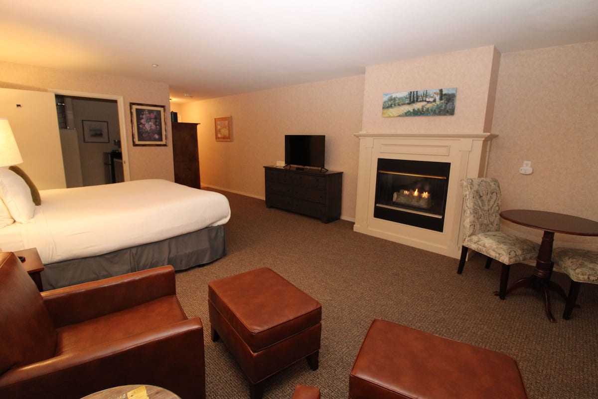 A hotel room with a bed, a dresser, a television, a fireplace, and a dining table with chairs.