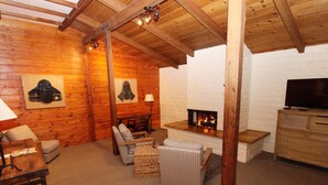 A cozy log cabin interior with a fireplace, wooden furniture, and a television. - Back Bay Inn (Los Osos)