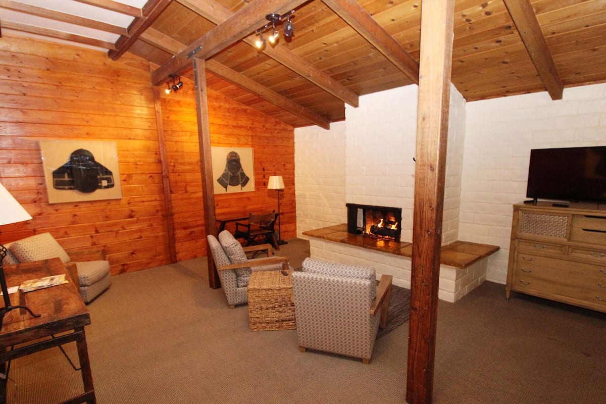 A cozy log cabin interior with a fireplace, wooden furniture, and a television.