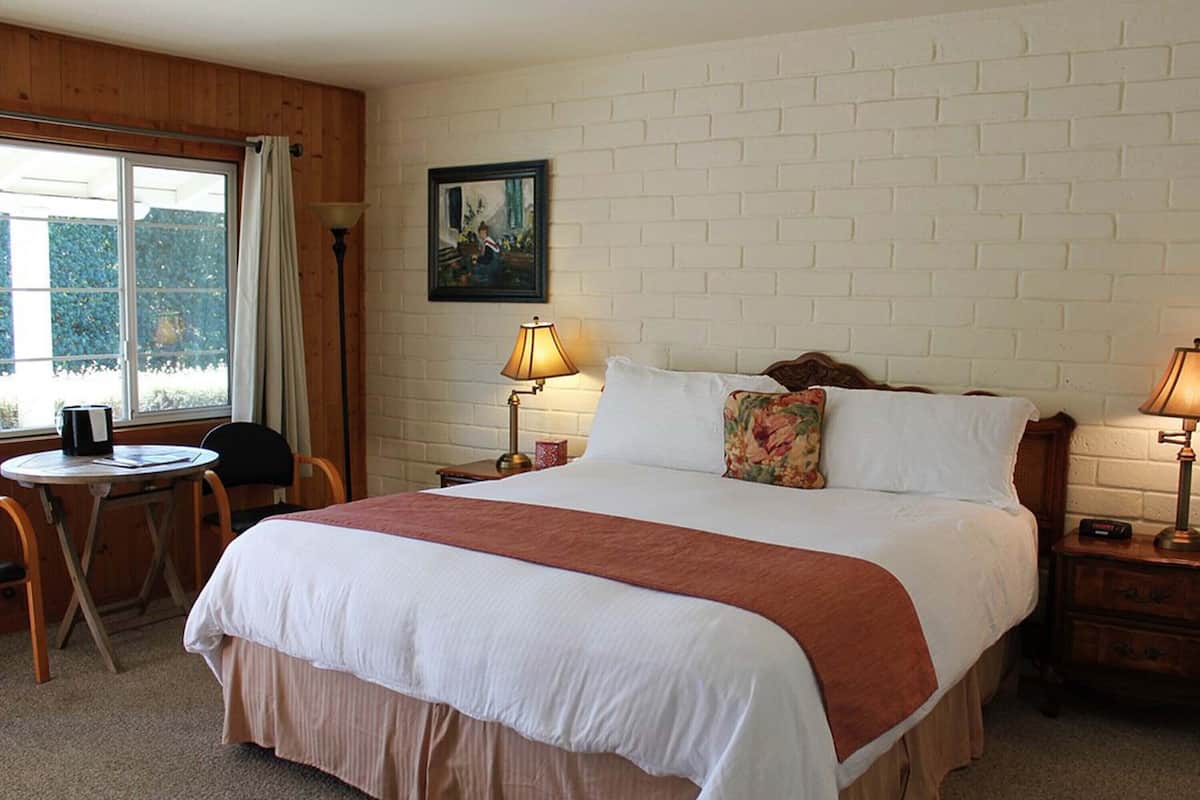 A hotel room with a large bed, a small table, a chair, a lamp, and a painting on the wall.