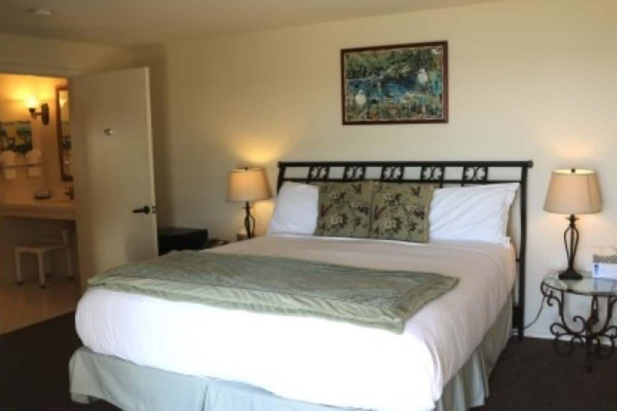 A hotel room with a bed, two bedside lamps, a painting on the wall, and a small table with a lamp.