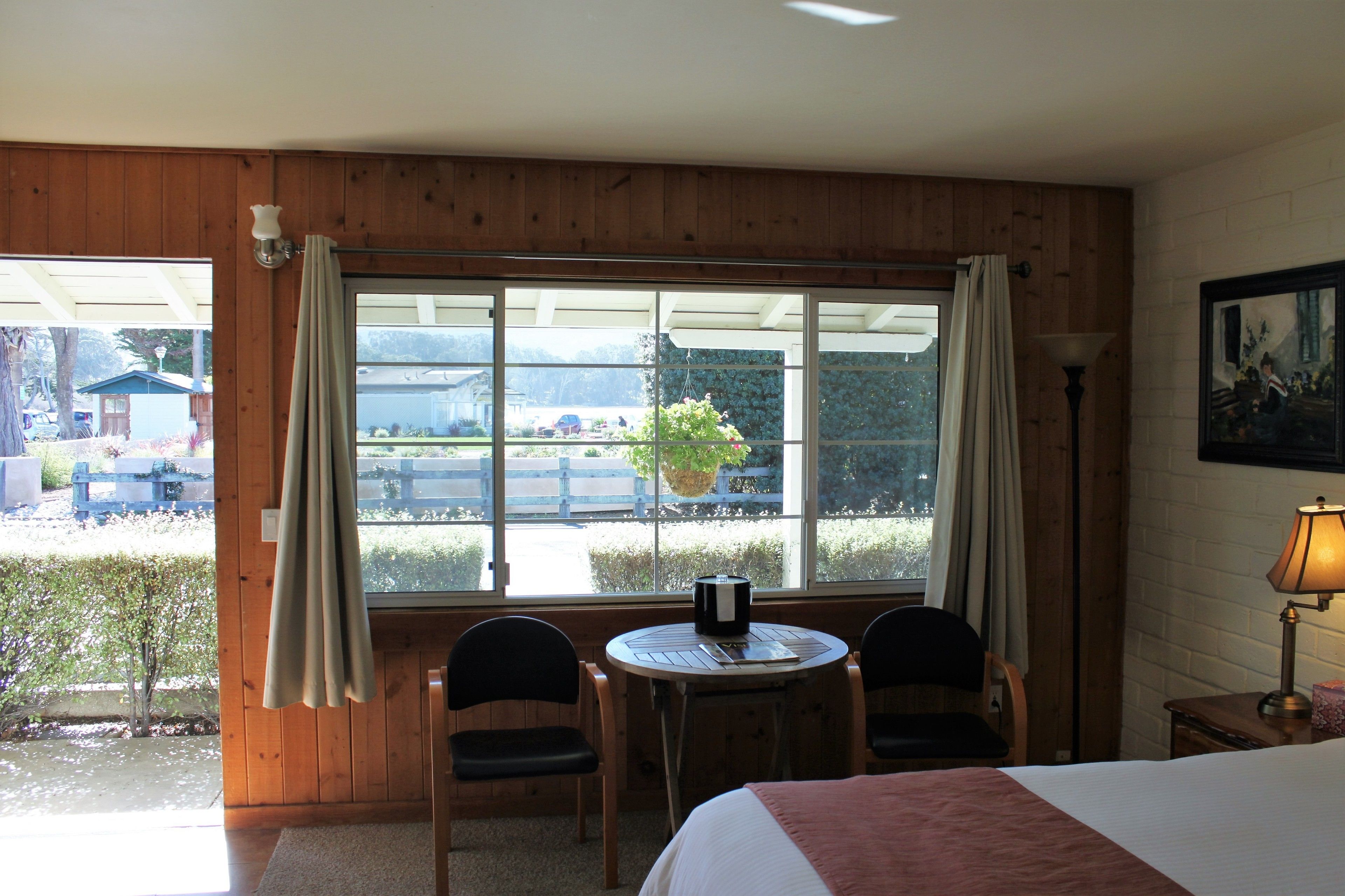 A room with a bed, a table with chairs, a window with curtains, and a lamp.