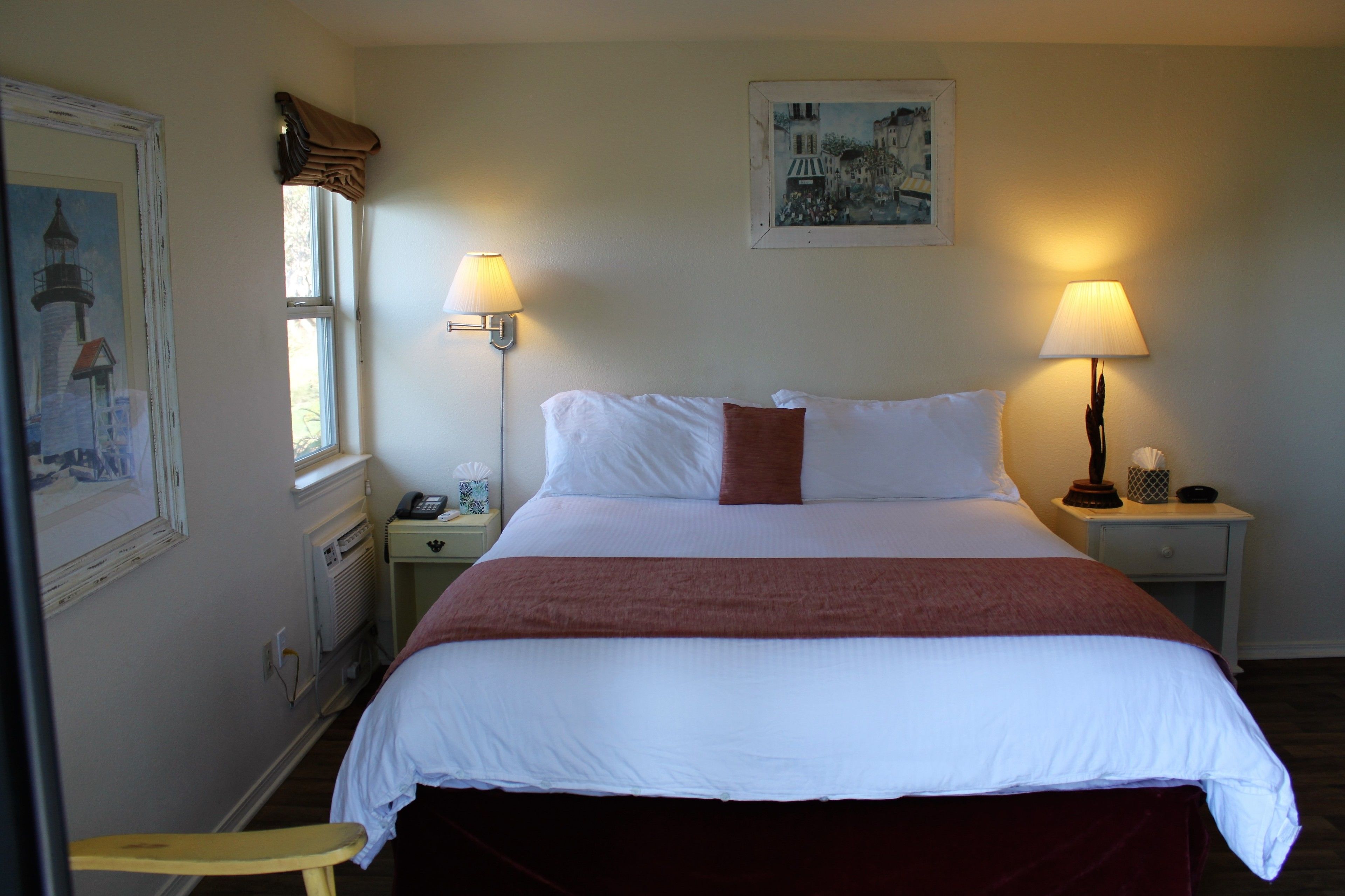 A neatly made bed with white and red bedding, two bedside lamps, a nightstand with a lamp, and a framed picture on the wall.