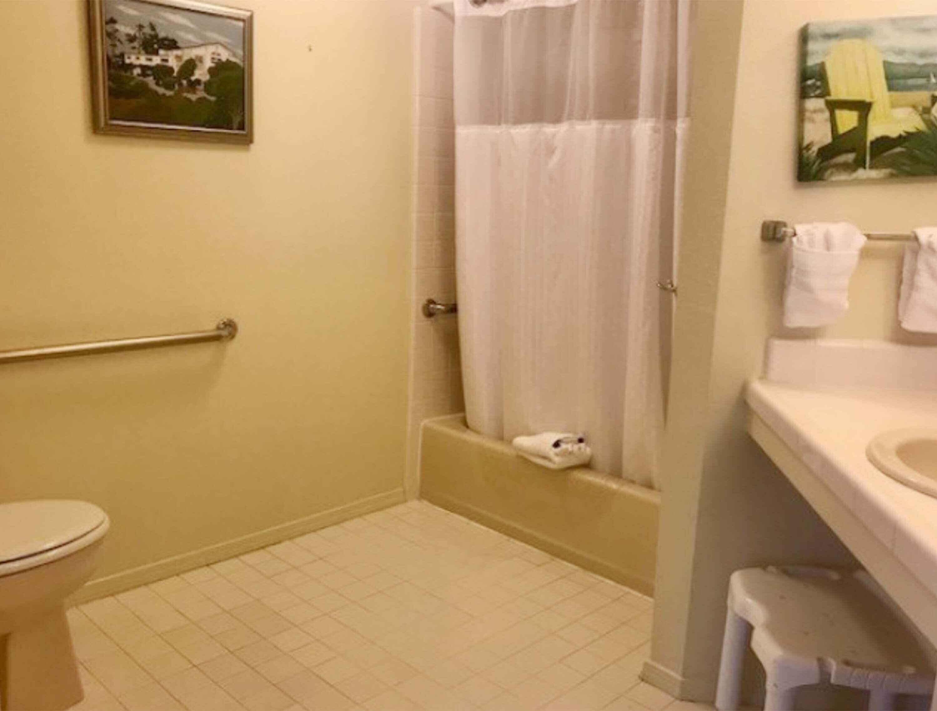A bathroom with a toilet, a shower with a curtain, a sink with a stool, and a towel rack.