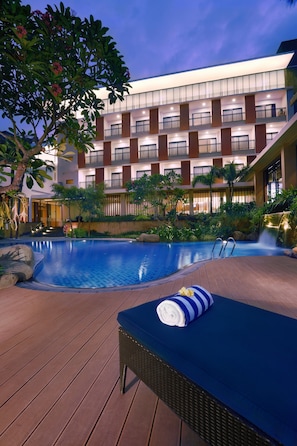 A modern hotel with a swimming pool, outdoor lounge area, and a waterfall feature.