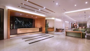 Een modern receptiegebied met een houten receptiebalie, een zithoek met groene banken en een decoratieve muur met bladmotieven.