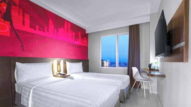 Habitación de hotel con dos camas, un escritorio, una silla, un televisor y vistas a la ciudad.